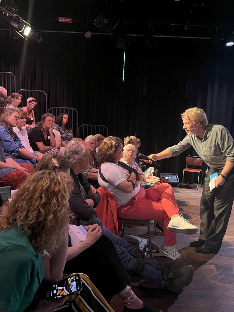 De gesprekleider haalt een ervaringsverhaal op uit het publiek tijdens de eerste editie van het INVOLV Theater